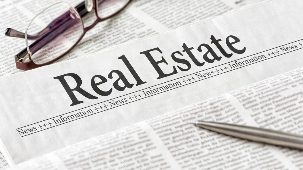 Glasses and a pen set on top of a newspaper page with the title Real Estate