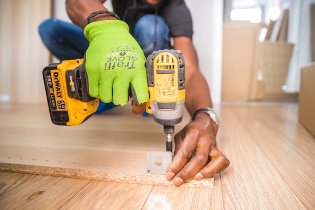 a man bent down drilling into a piece of wood inside a home
